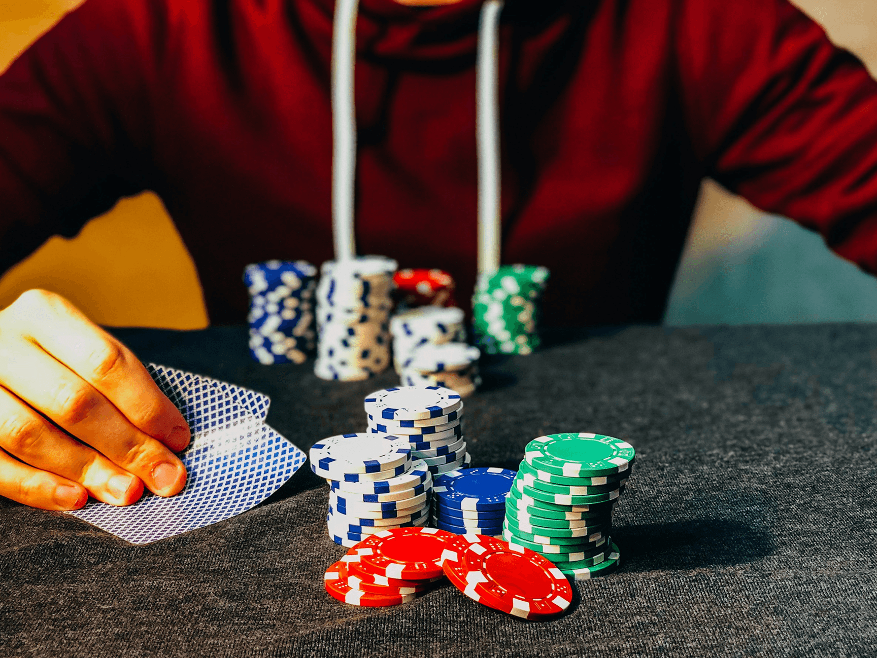 Fichas de poker e pessoa ao fundo segurando cartas